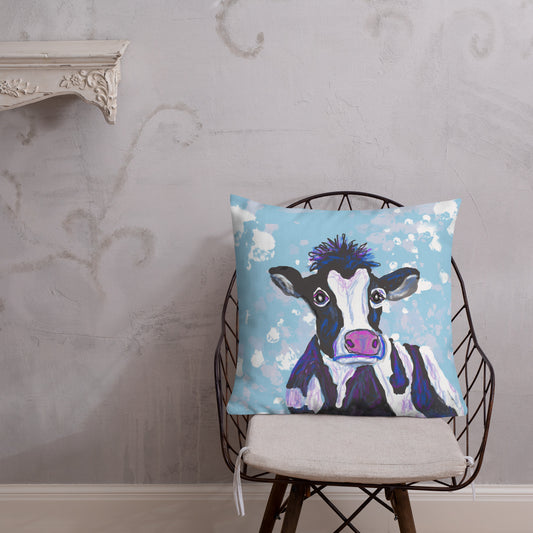 Soulful cow, symbol of the Mother Goddess adorns throw pillow. Black and white cow with pink-purple nose against a blue sky dotted with clouds. Sits on a chair. 22x22