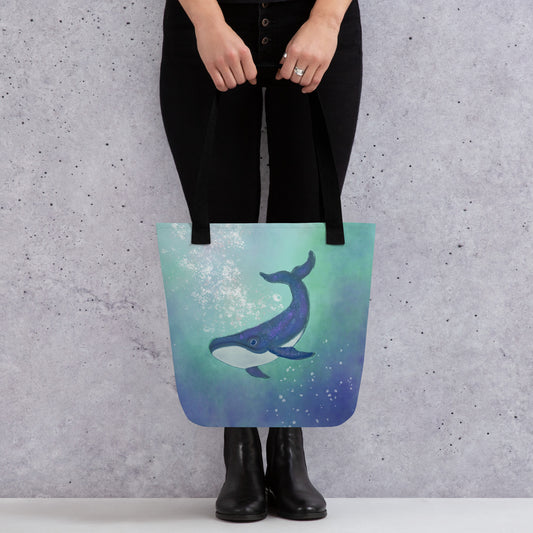 Tote bag with a artist's whale design held by a person against a gray wall. Symbol deep wisdom, emotional depth, and inner truth.