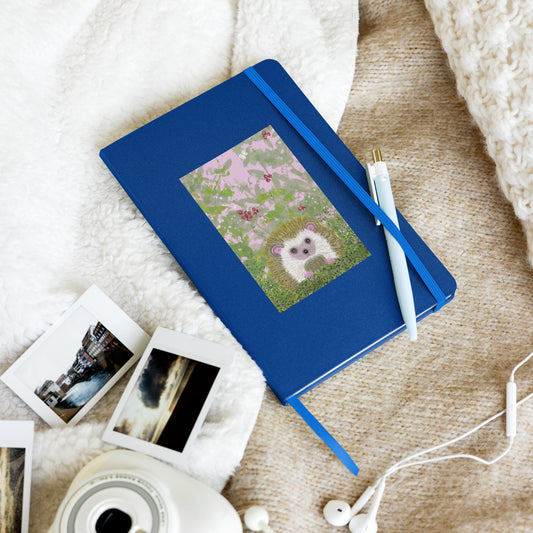 Hardcover notebook with an image of a hedgehog on the cover. The garden animal in the image sits in brambles--vines and berries and a white butterfly. Notebook shows a pen held by the elastic closure.