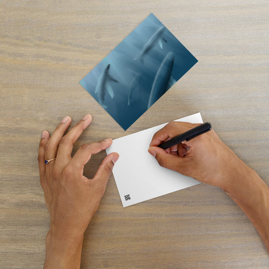 Person holding a pen over a postard with an image of a pod of whales.