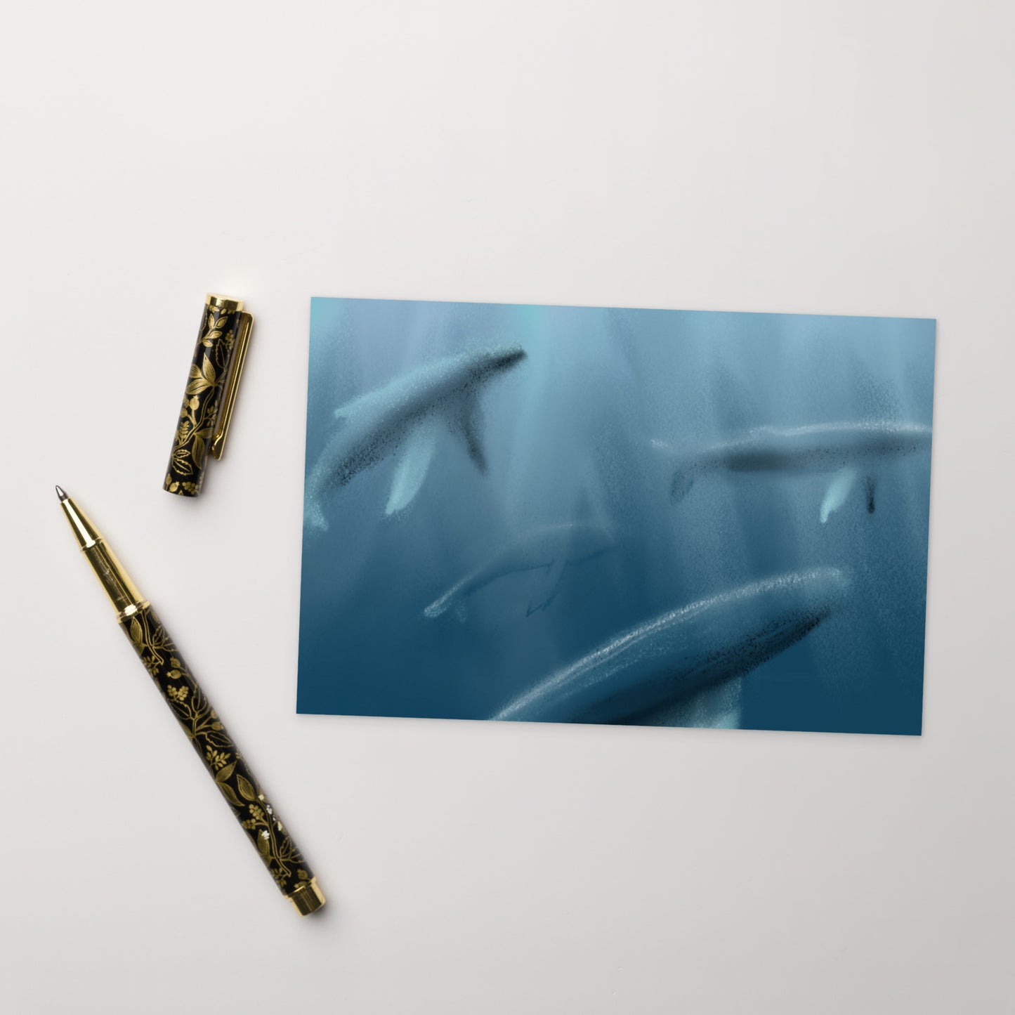 Decorative pen on a white surface with a blue card featuring a pod of whales.