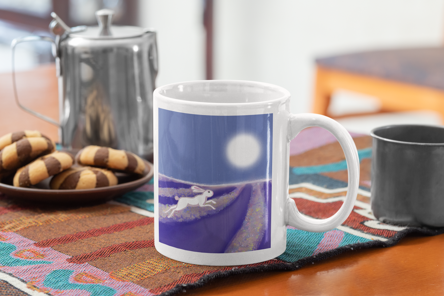 Mug with a hare running througj a of lavender under a full moon on a table with cookies and a teapot.