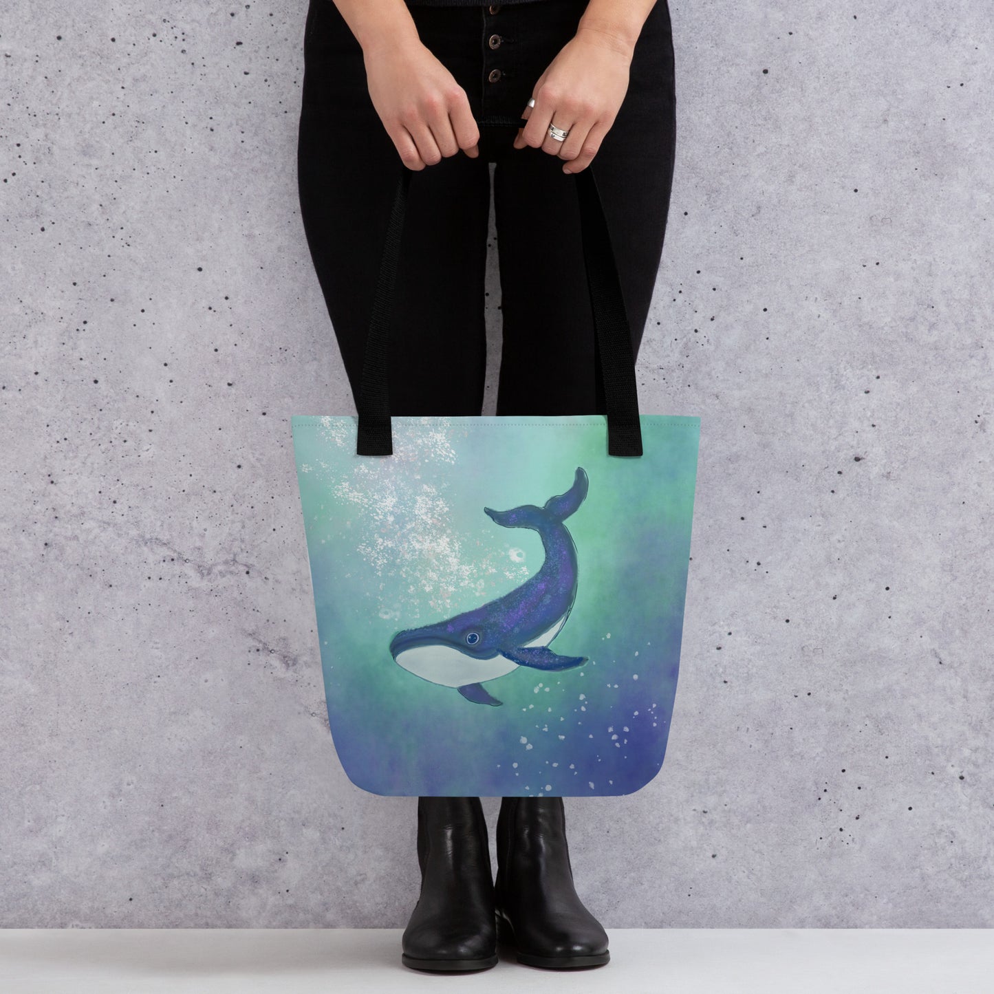 Tote bag with a artist's whale design held by a person against a gray wall. Symbol deep wisdom, emotional depth, and inner truth.