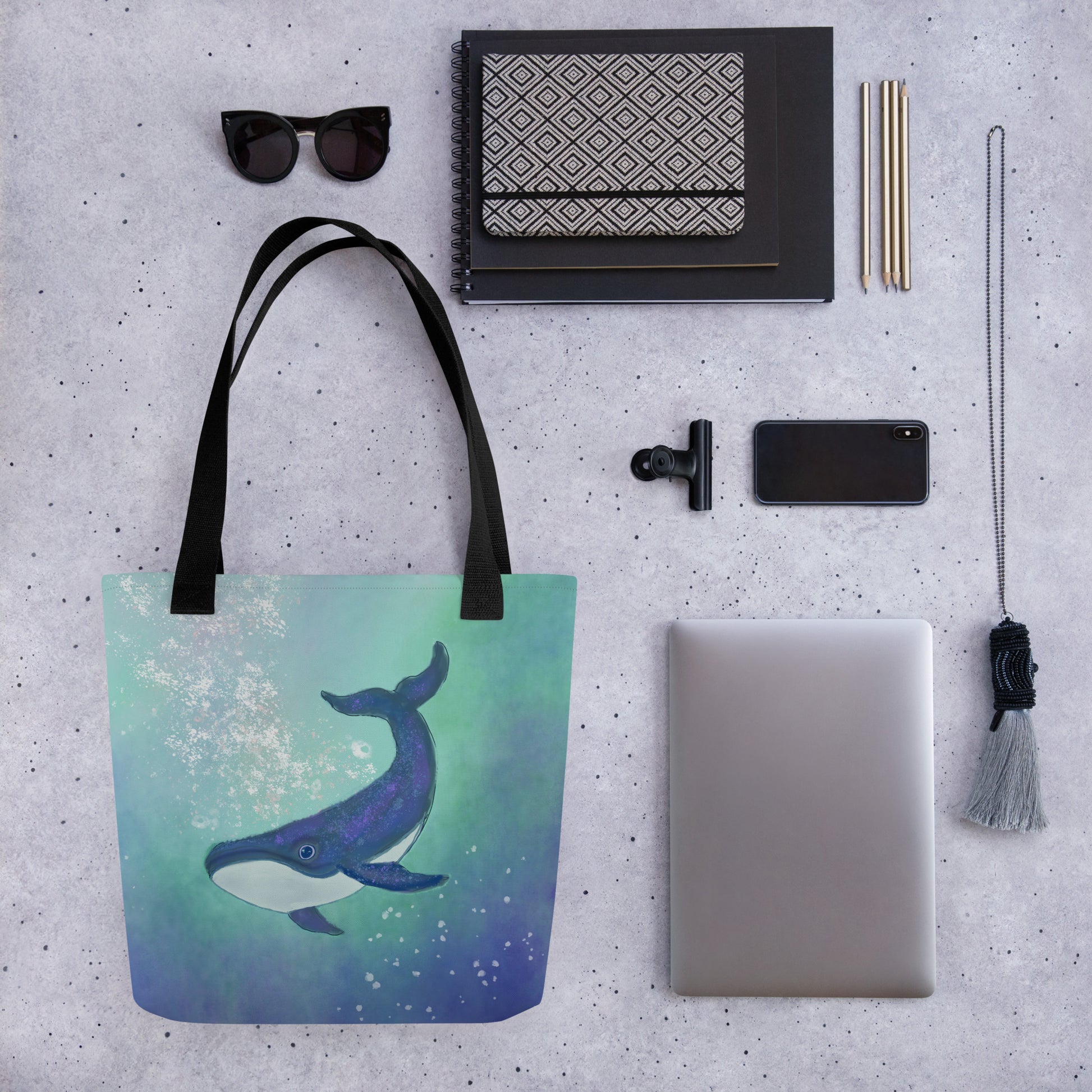 Tote bag with whale design on a gray surface with various items it light carry.