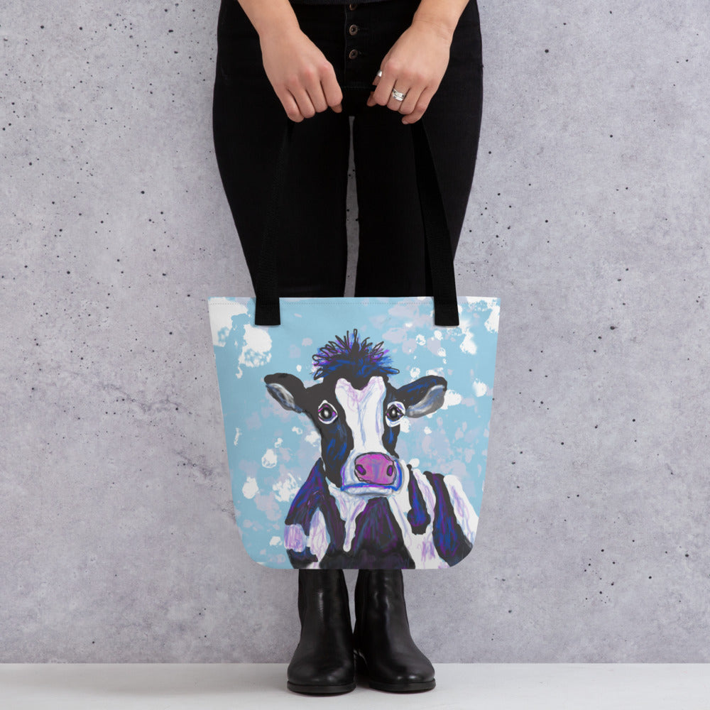 A tote bag to carry everything you need from office to the beach.  Image of a black and white cow with a pink nose against a blue sky.