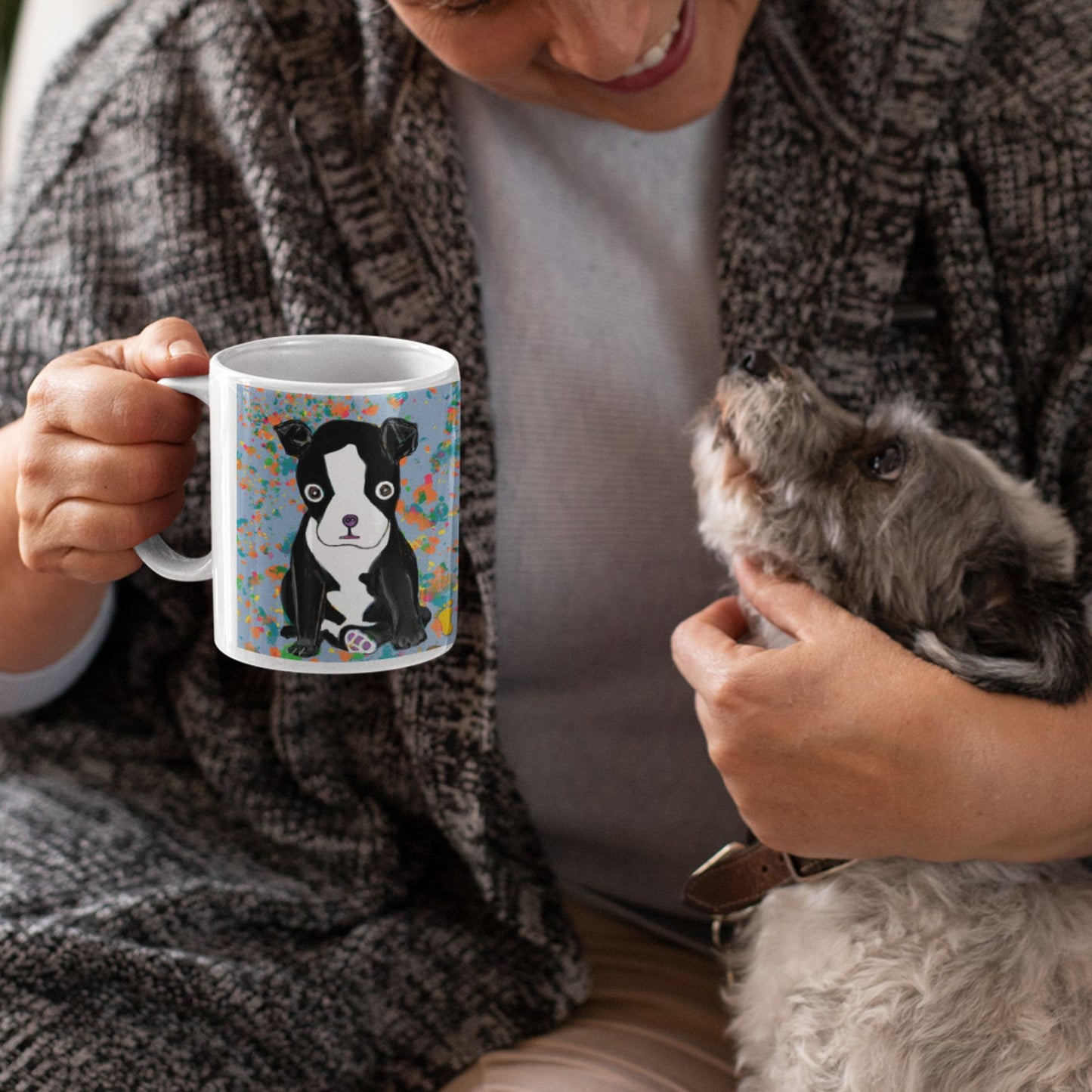 Person holding a ceramic Boston Terrier spirit mug with a dog design and a dog in their other hand