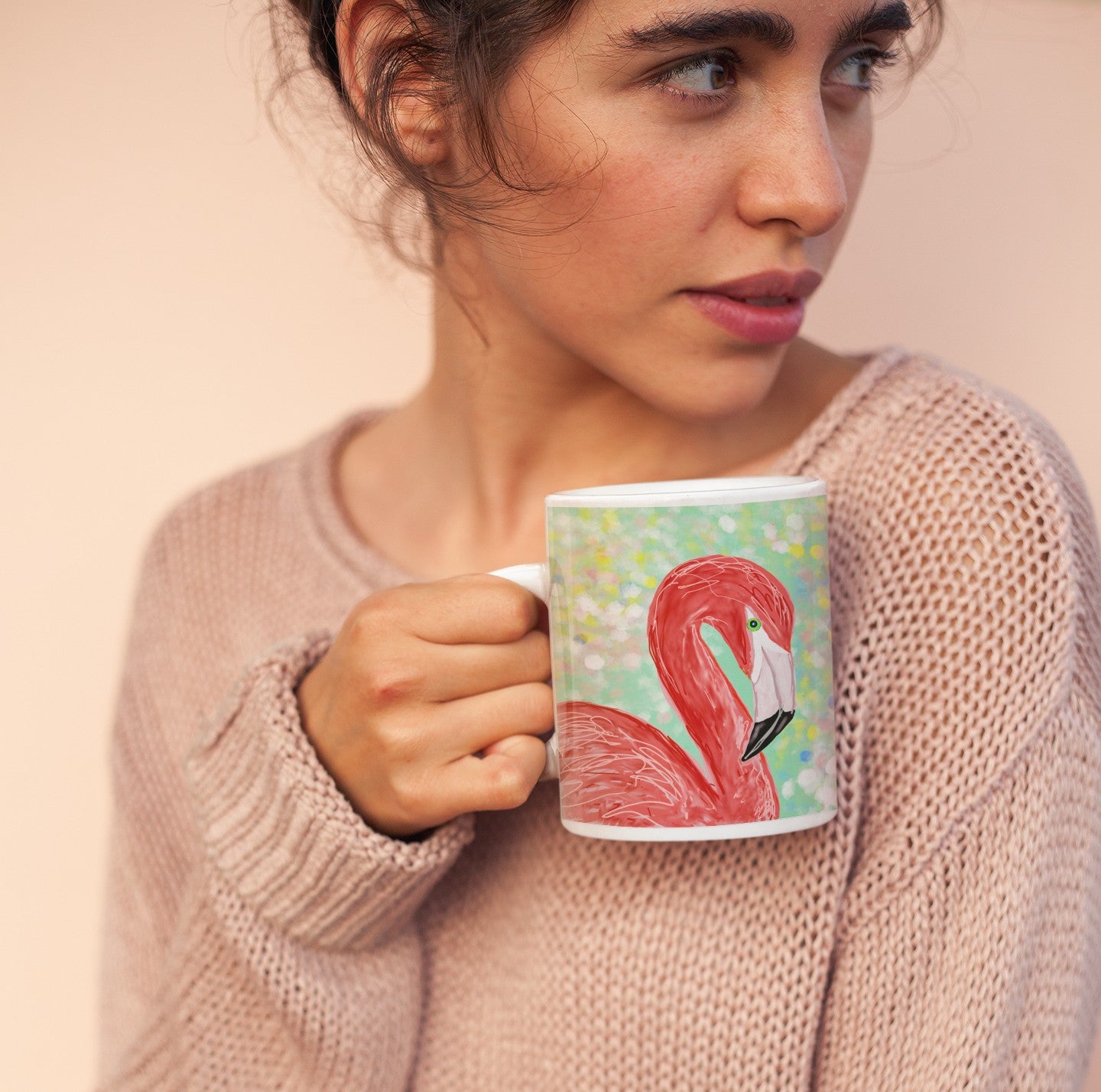 Woman holding a mug with a flamingo design against a plain background