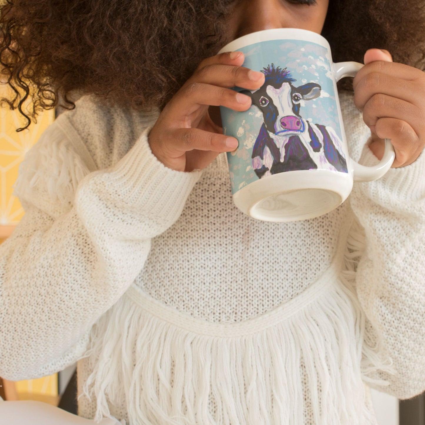 Person holding a  spirit mug with a cow design, wearing a white sweater.