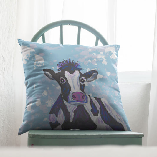 Decorative pillow with a cow design on a light blue background, placed on a green chair.