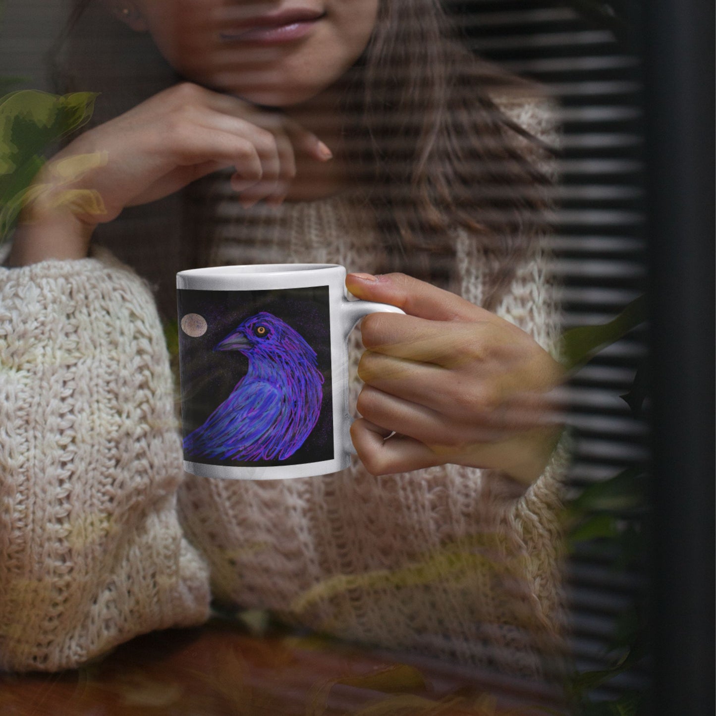 Person holding a mug with an original  Crow design, while looking at a window.