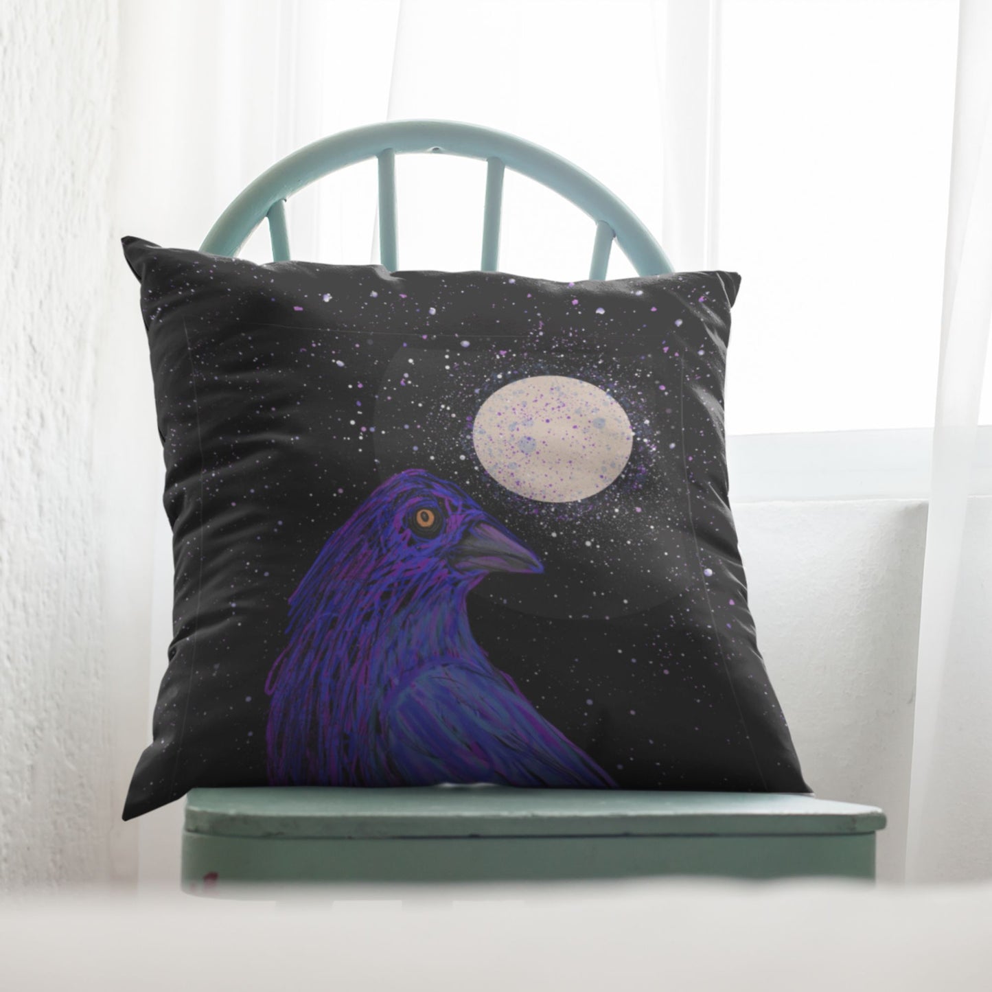 Decorative pillow with a golden-eyed crow and moon on a starry night, placed on a light blue chair.