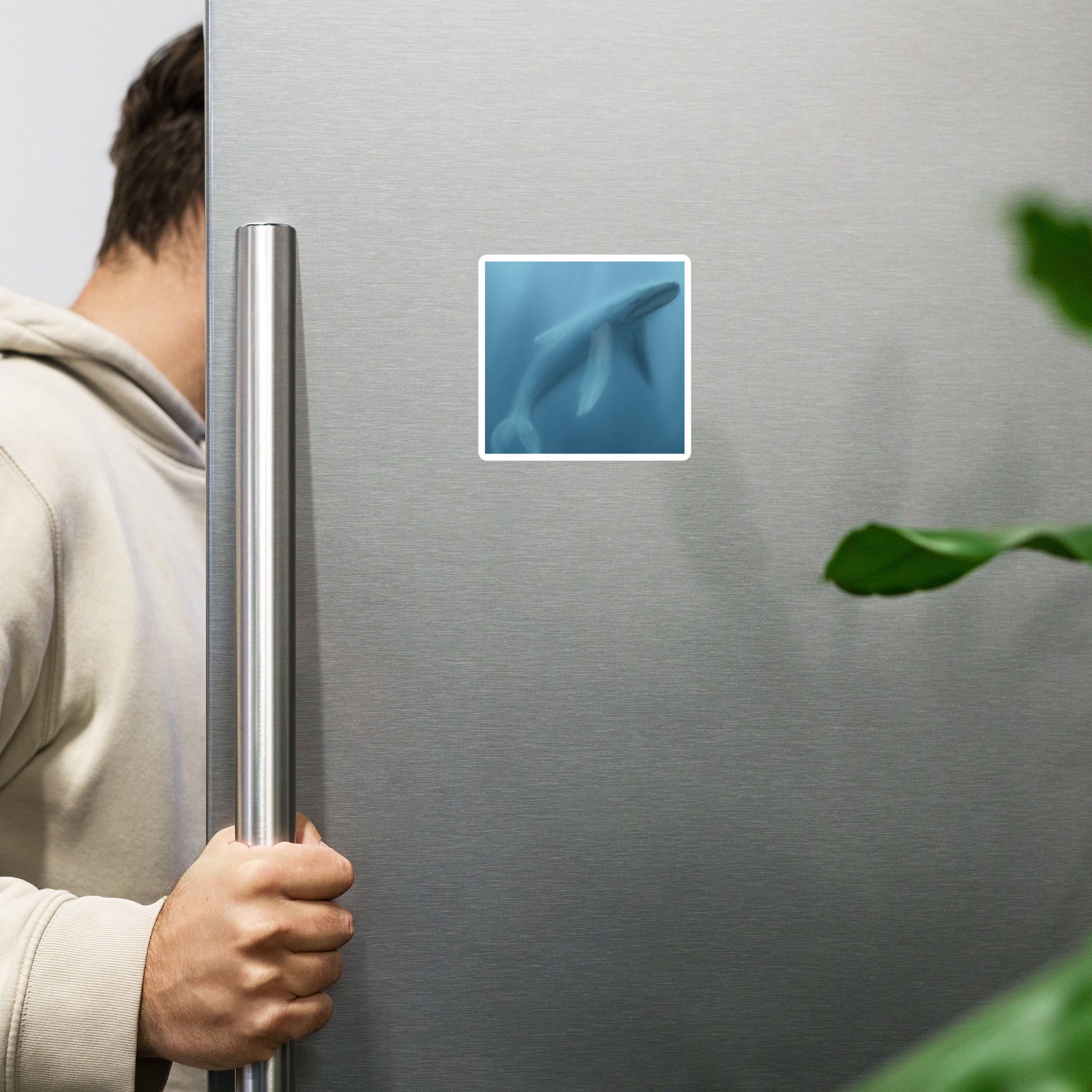 Person opening a silver refrigerator with a magnet with image of a whale swimming in the deep.