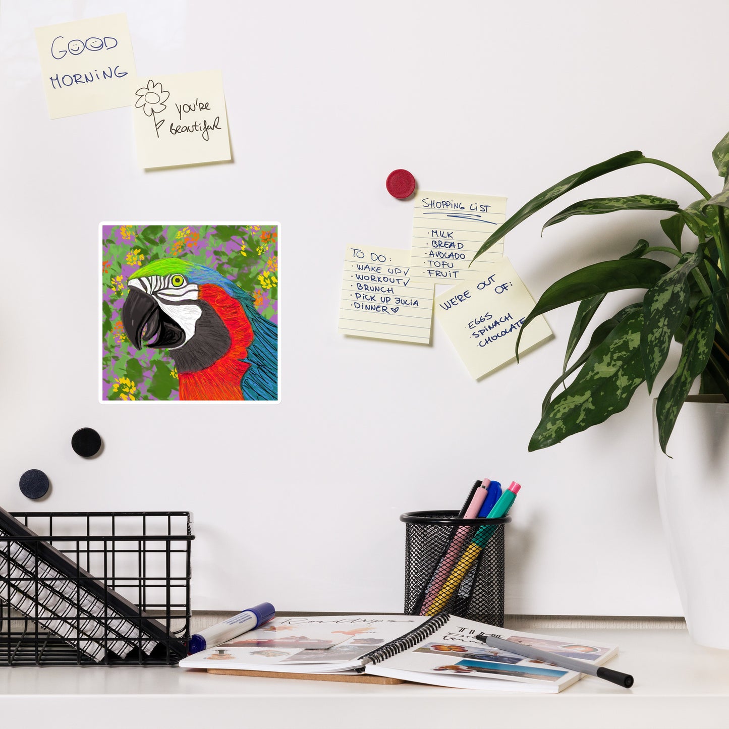 Desk with a colorful parrot magnet , notes, and stationery items on a white board.