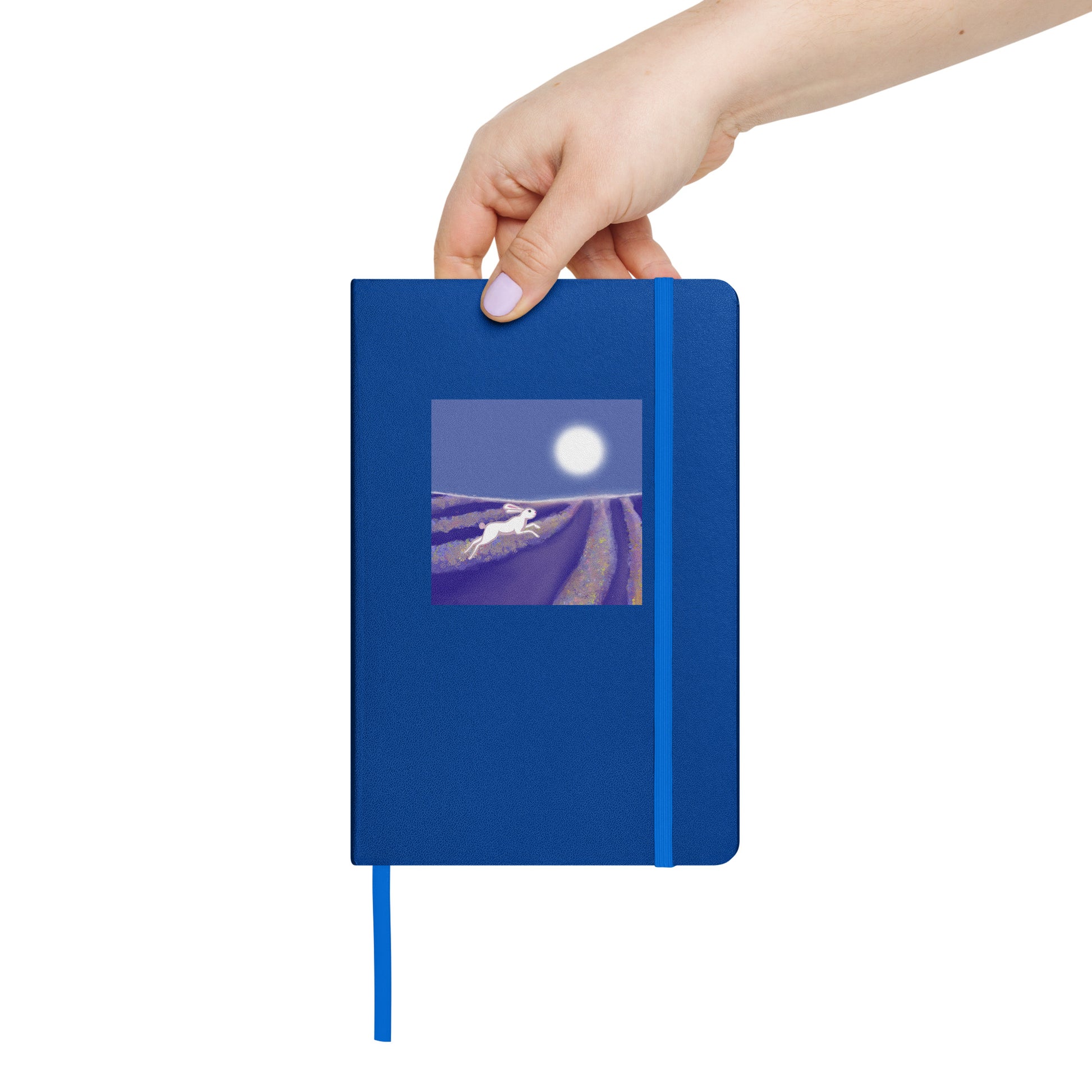 Hand holding a blue notebook with a hare running through lavender fields cover design