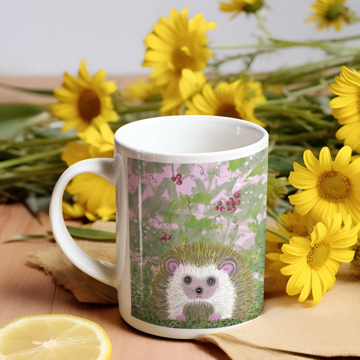 White mug with a hedgehog design surrounded by yellow flowers on a table.