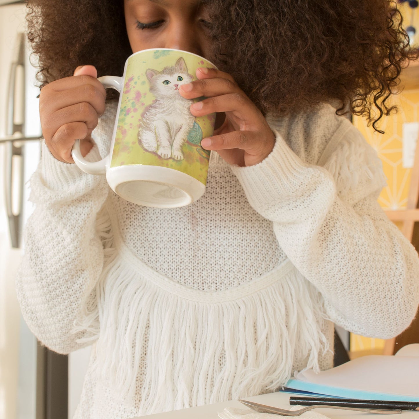 Young girl wearing a white sweater holding a kitten spirit mug with an original kitten design.