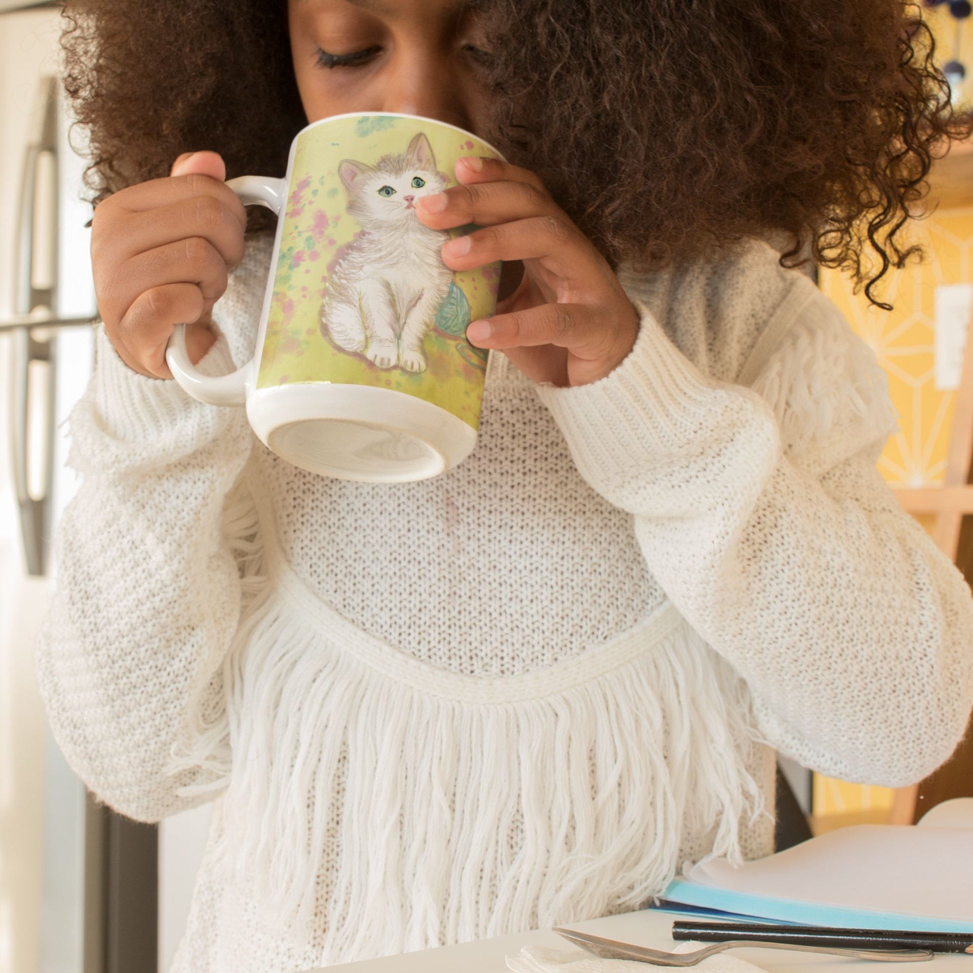 Young girl wearing a white sweater holding a kitten spirit mug with an original kitten design.