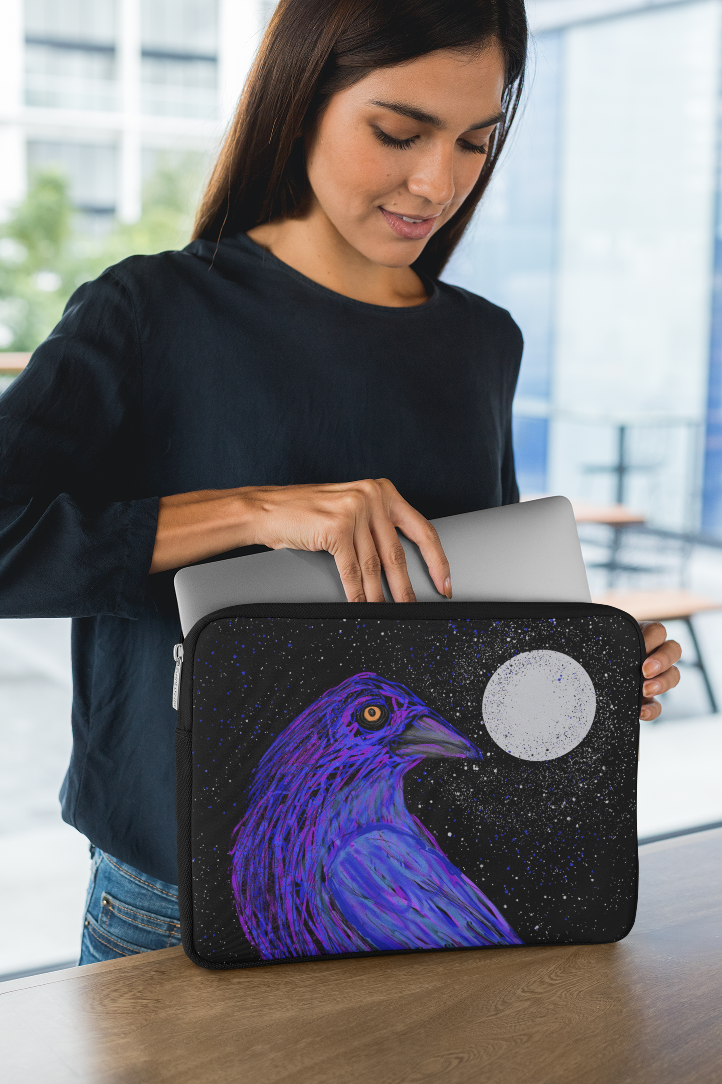 A woman puts her laptop into the Crow sleeve, taking her spirit animal to work with her.