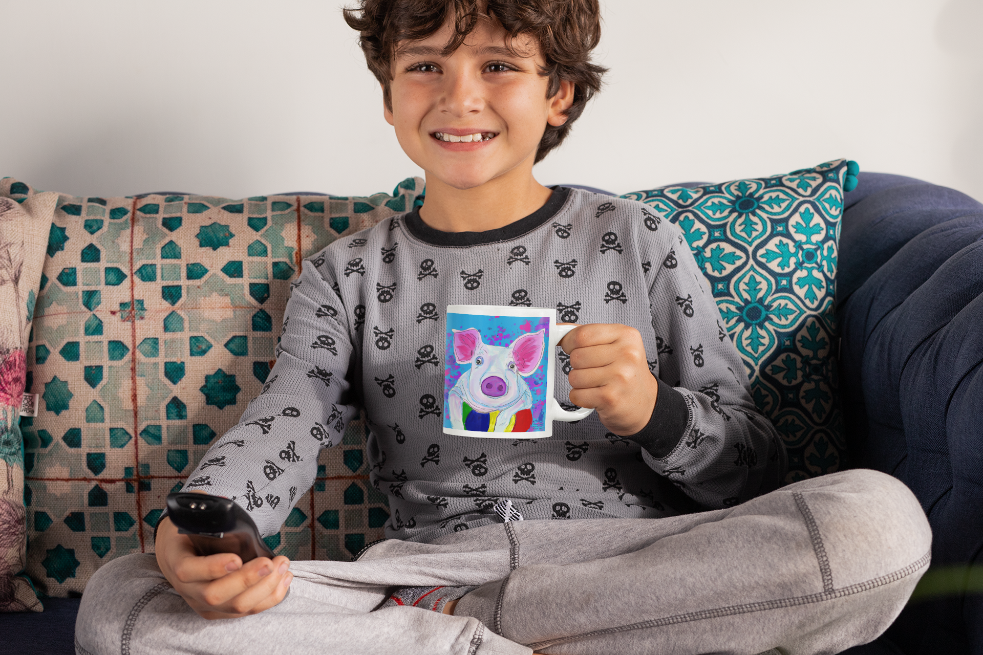 Child sitting on a couch holding a remote control and a mug with a colorful Pig on it.