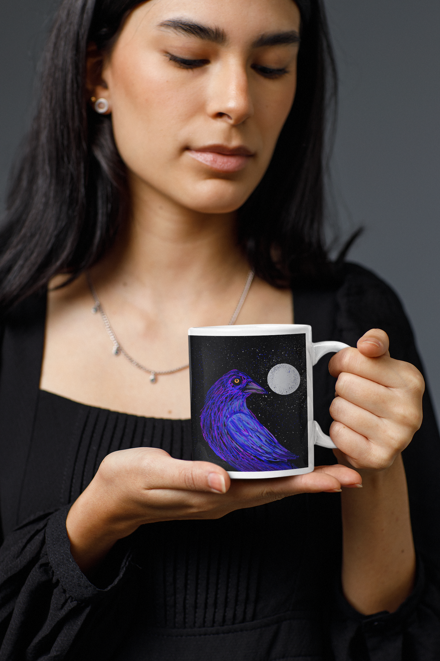 Woman dressed in black holding a mug with a Crow Spirit perched under a full moon against a dark background
