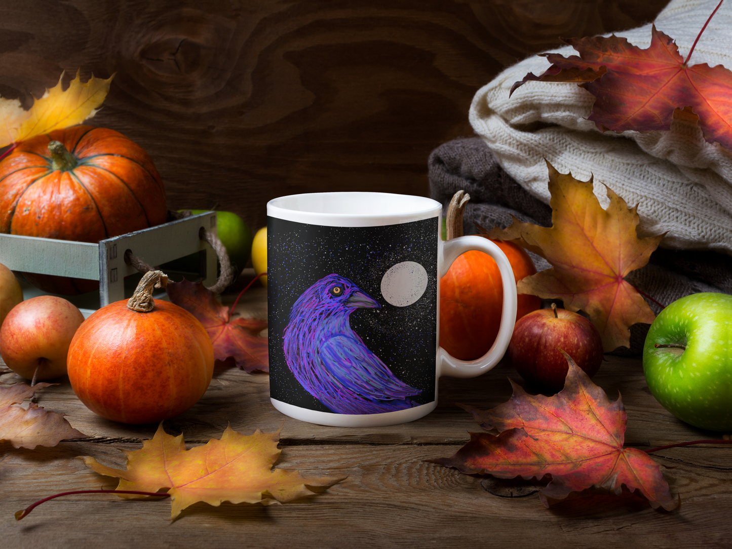 Mug with a Crow under a full moon and a star filled sky sits on a wooden table set for fall with fall leaves, pumpkins and apples.