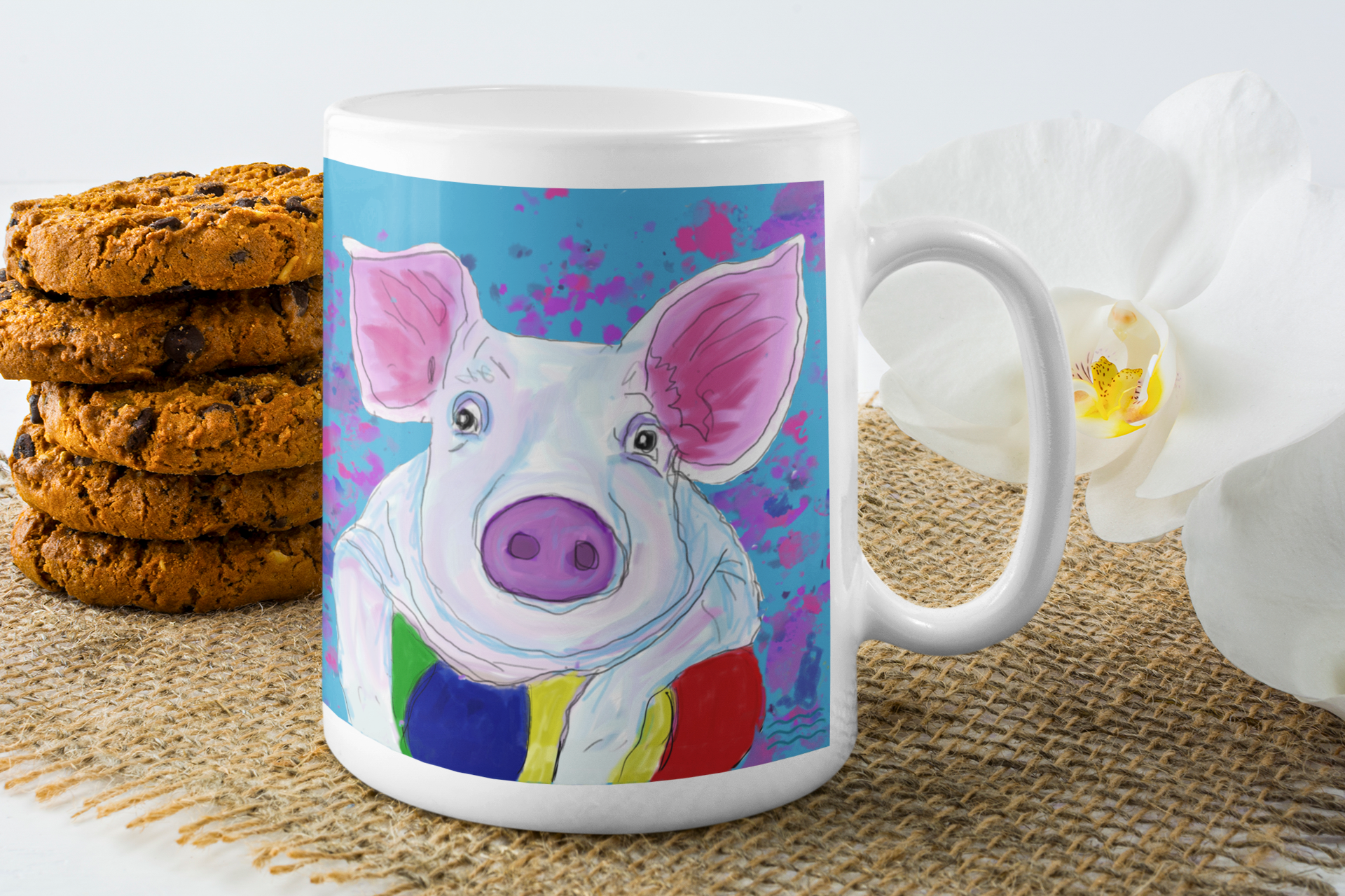 Mug with a colorful pig design on a table with cookies and flowers