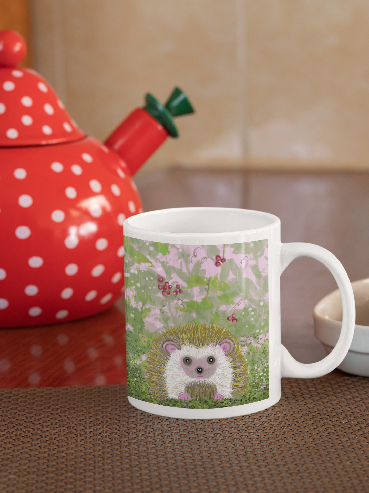 Mug with a hedgehog design in a kitchen setting with a red polka dot teapot. The hedgehog is in a green bush with red berries.