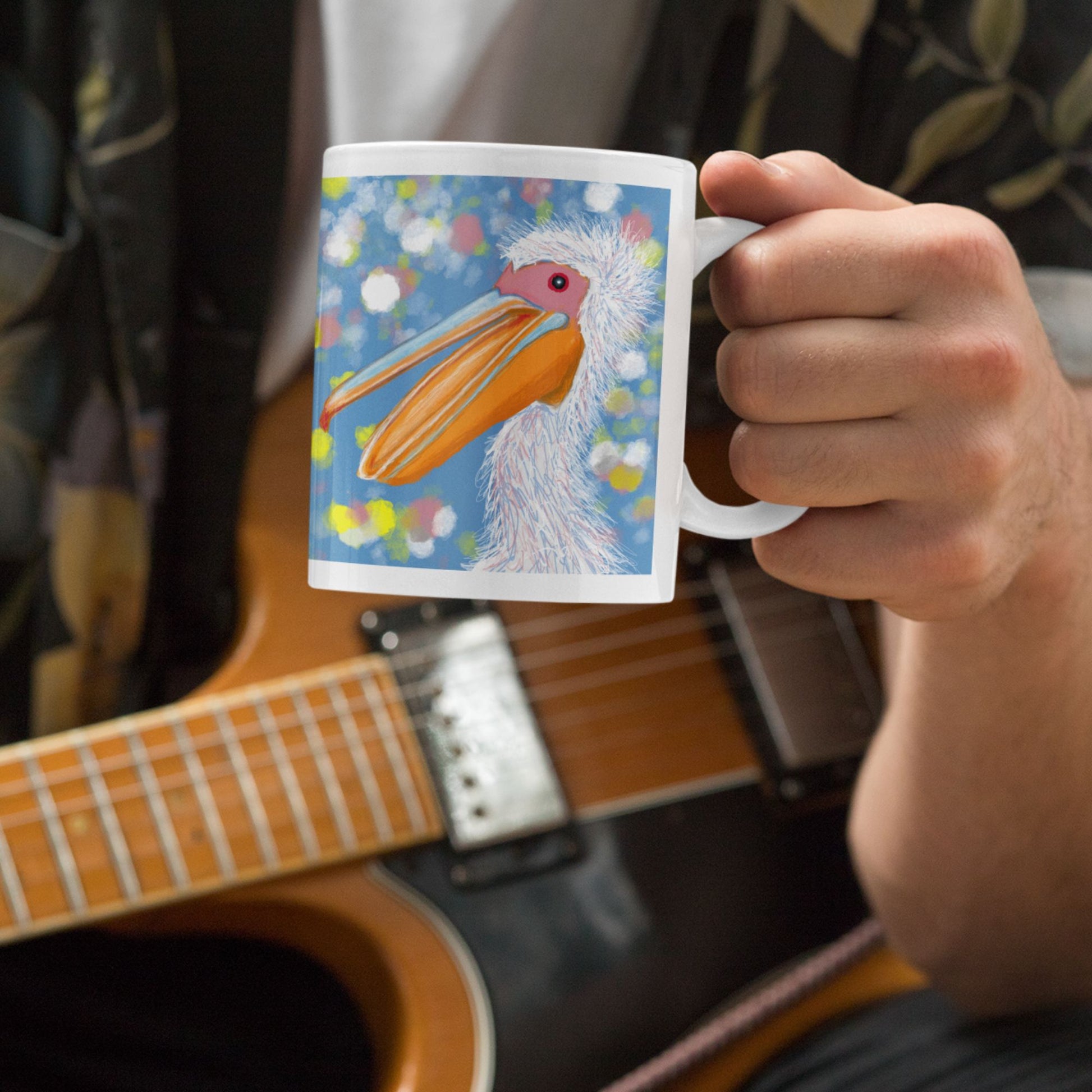 Person holding a pelican spirit mug with an original  design in front of an acoustic guitar.