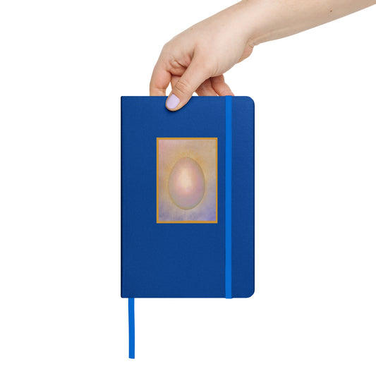 Hand holding a blue notebook with a original artists design of a penguin egg on the cover against a white background