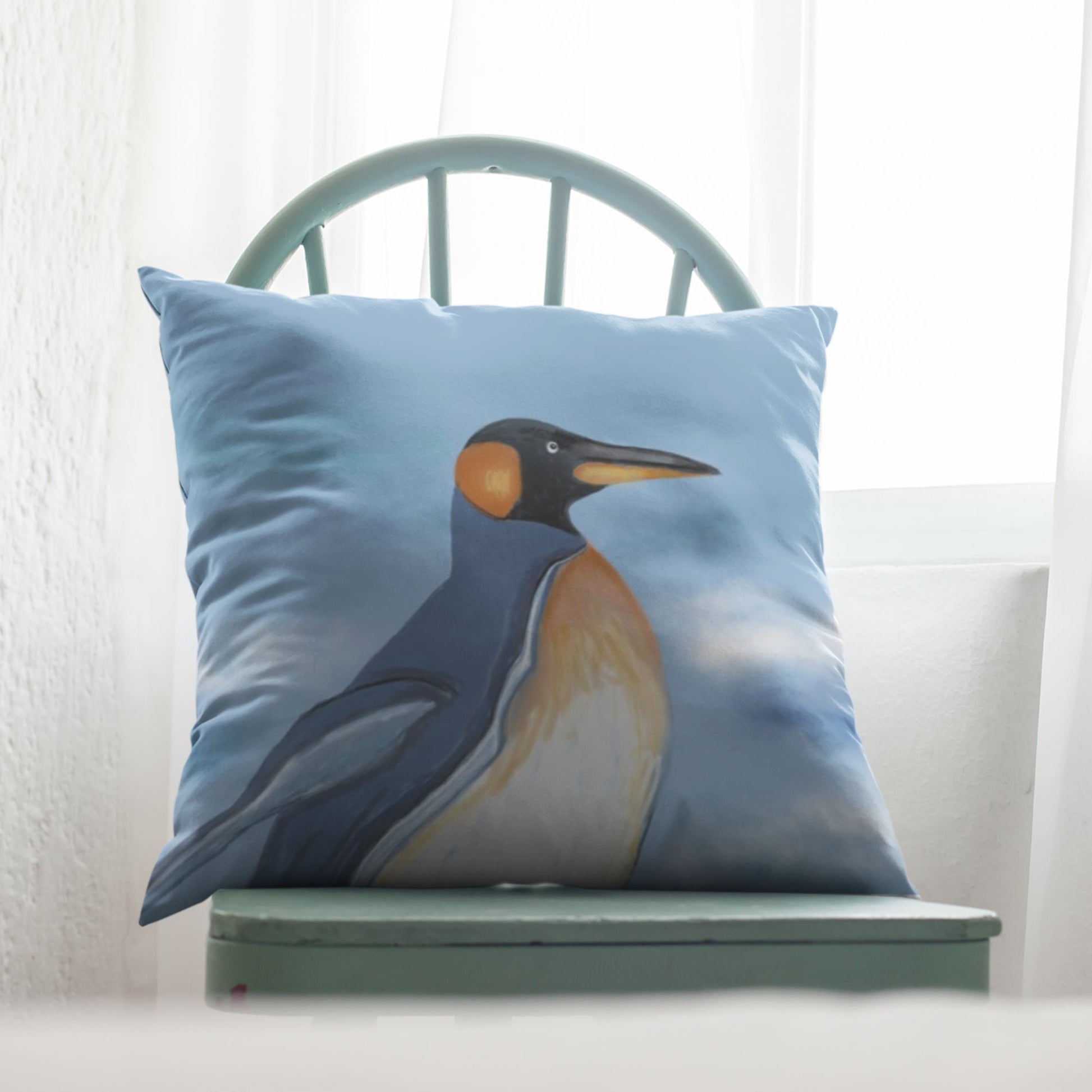 Pillow with a penguin design on a green chair against a white curtain background