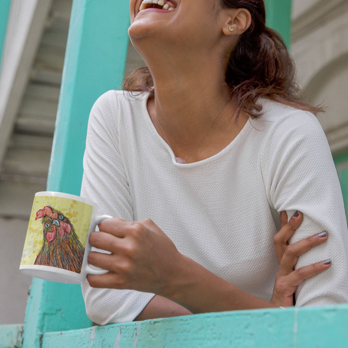 Woman holding a mug with a rooster design, laughing on a balcony.