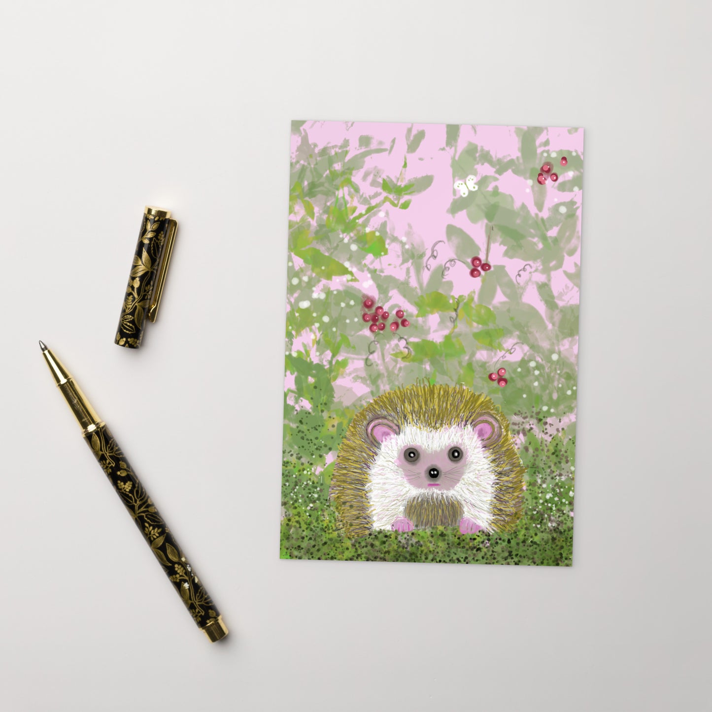 Sweet postcard with an image of the garden animal, the hedgehog.  Image shows hedgehog in a bramble of vines and berries, with a white moth. Hedgehog, with his sweet face, is gentle and kind spirit animal / spirit guide connected to Mother Earth. Standard size postcard, vertical alignment. Shown next to pen and pen cap.