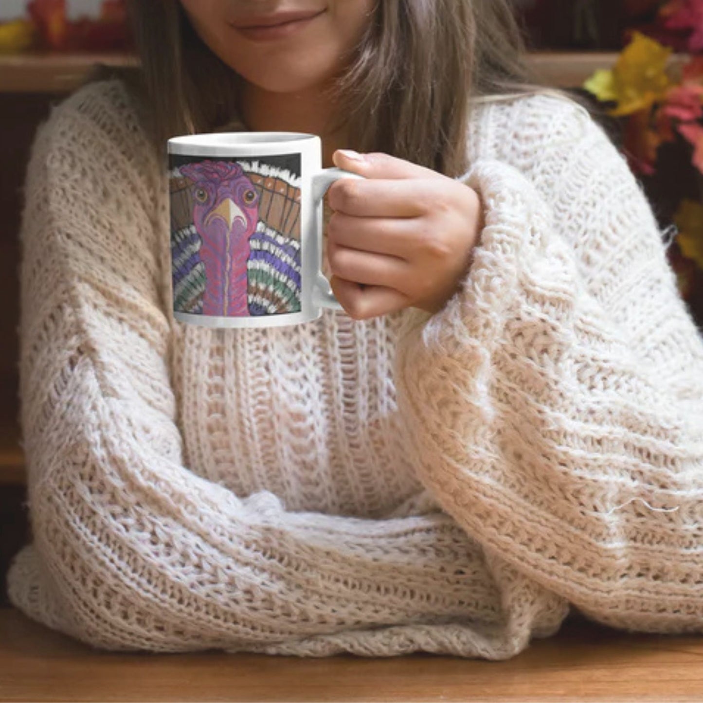 A woman in a cosy beige sweater holding a ceramic turkey spirit mug with an original artist's design.