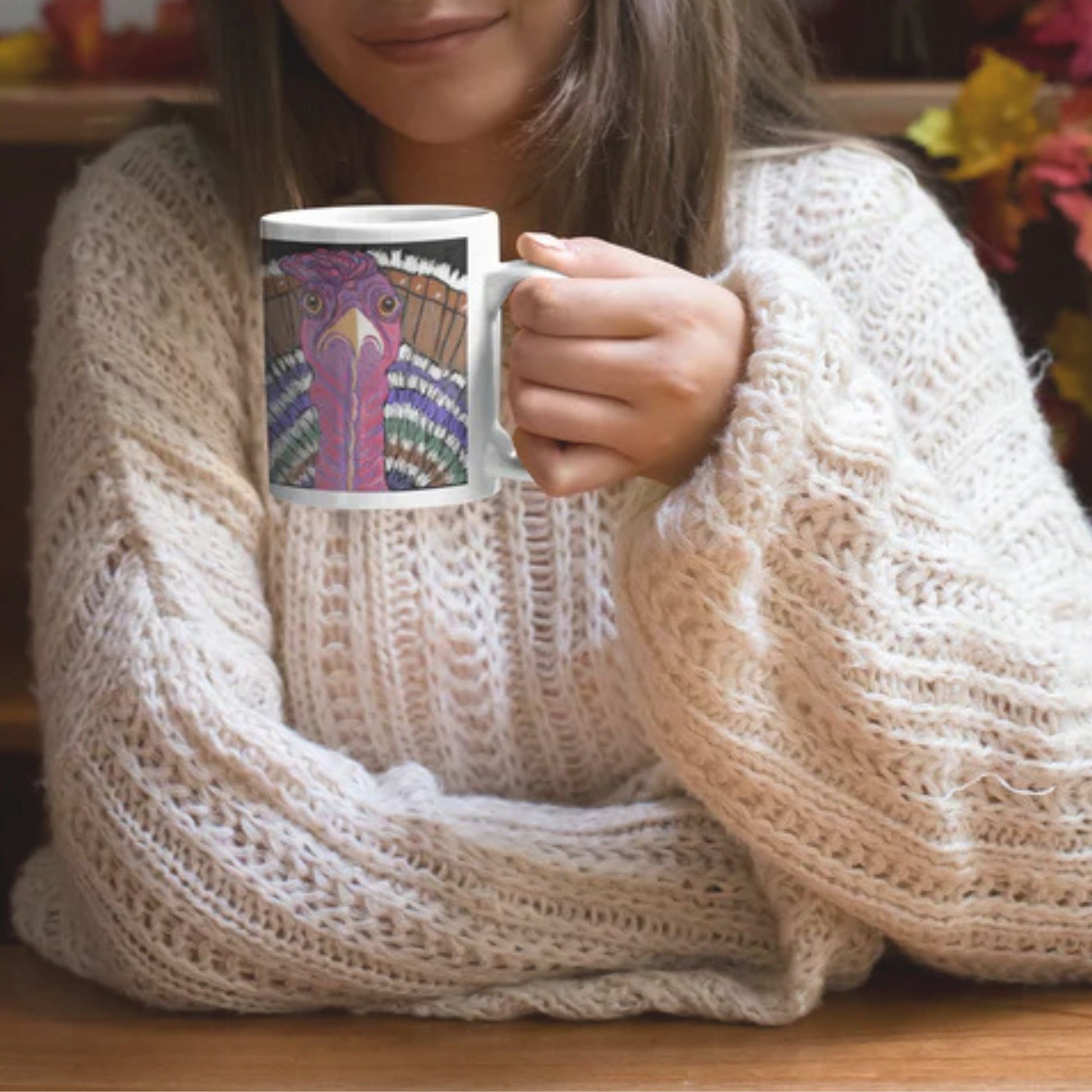 A woman in a cosy beige sweater holding a ceramic turkey spirit mug with an original artist's design.