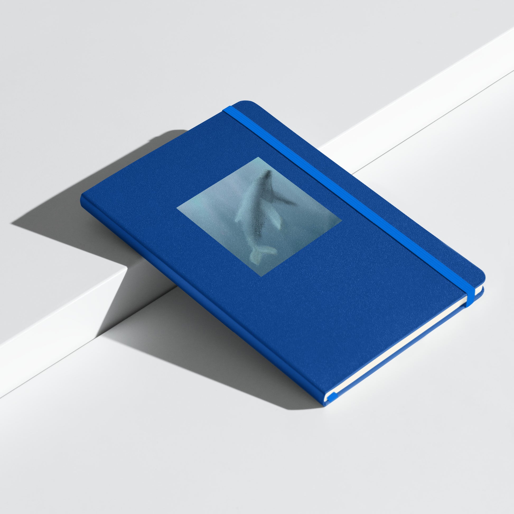 Blue notebook/journal with an artist's image of a whale on the cover, showing an elastic closure. 