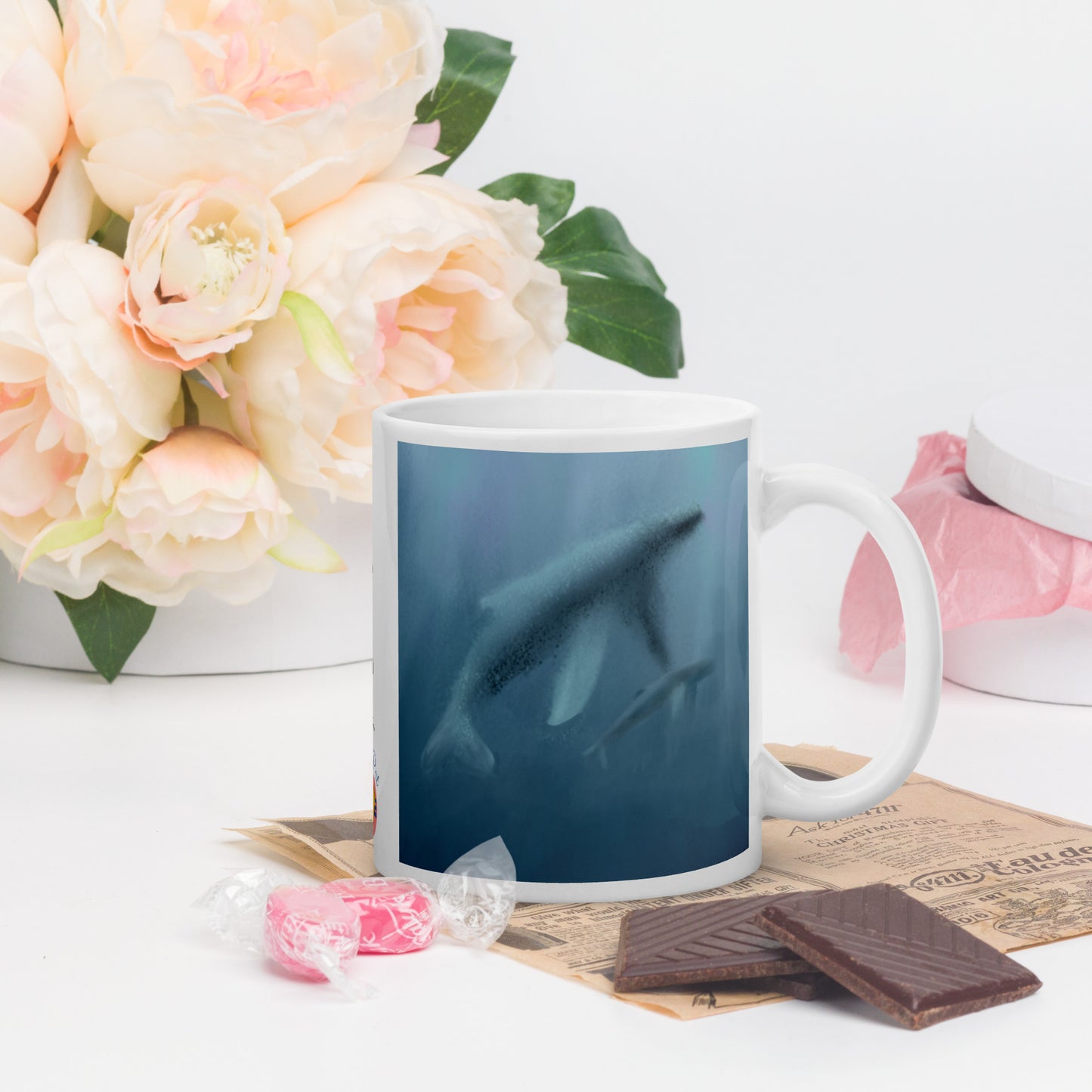Mug with a whale design on a table with flowers and chocolate. Misty blues showing mother and calf.