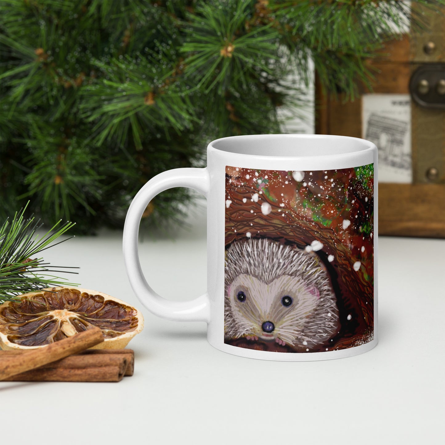 White mug with a hibernating hedgehog design on a table with winter decorations.