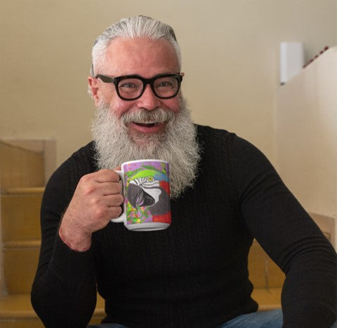 Is the parrot your spirit animal? Smiling gray-haired, bearded man wearing a black sweater and glasses holding a large, brightly colored white ceramic mug with a parrot on a field of purple and green.