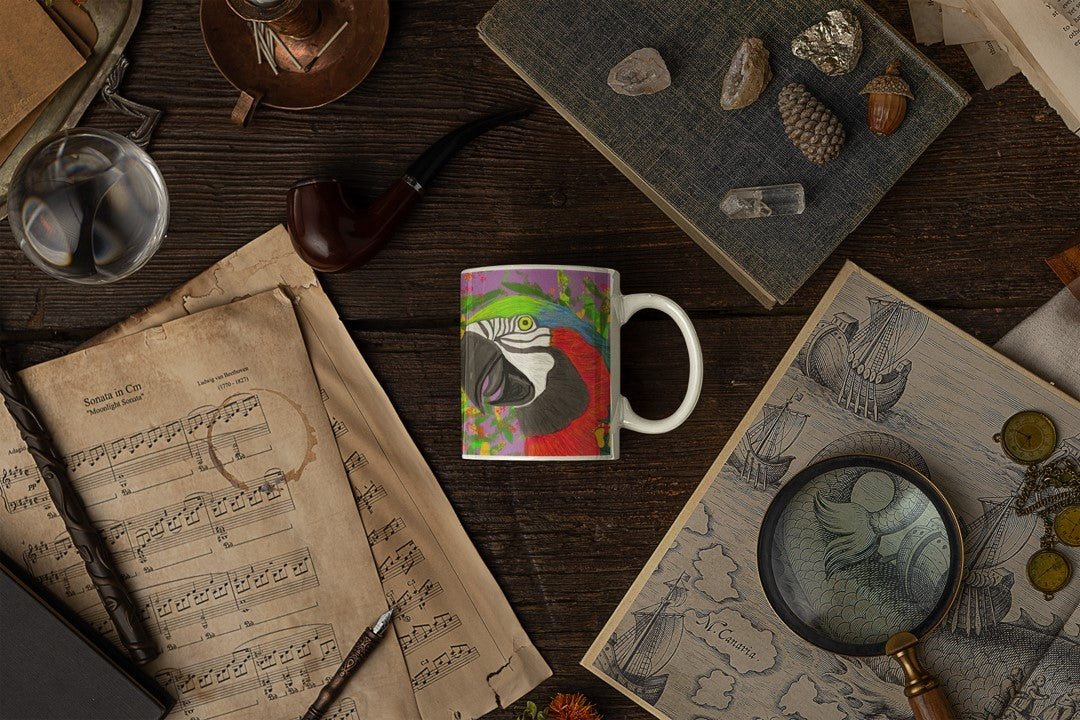 Brightly colored white ceramic mug with a parrot on a field of purple and green, front view on a dark table with sheet music, crystals, a map and a magnifying glass