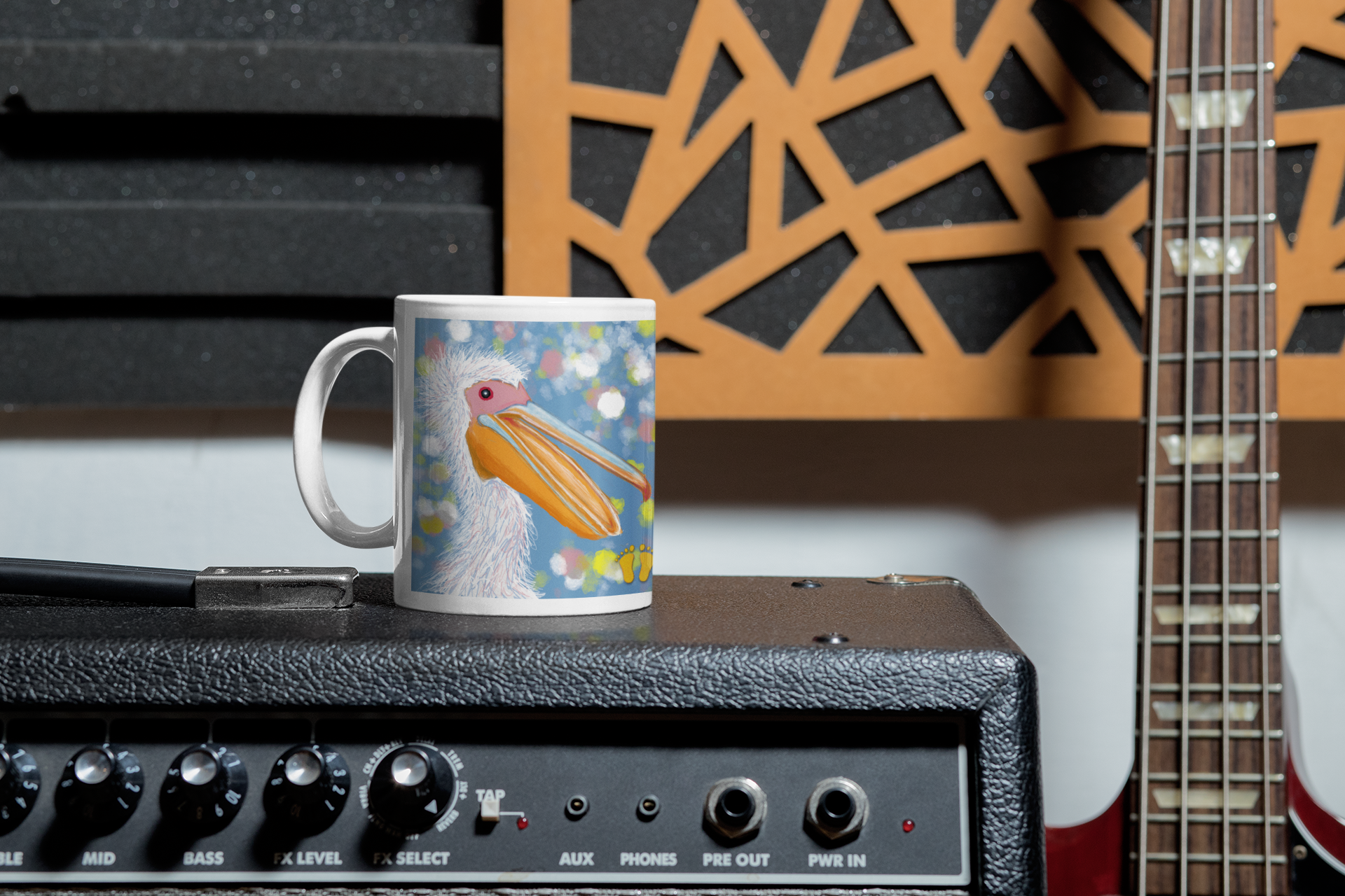 Premium ceramic coffee mug is a unique gift for bird lovers. Brightly colored pelican is on a field of blue with accents of white and yellow. Shown here on an amplifier with a guitar.