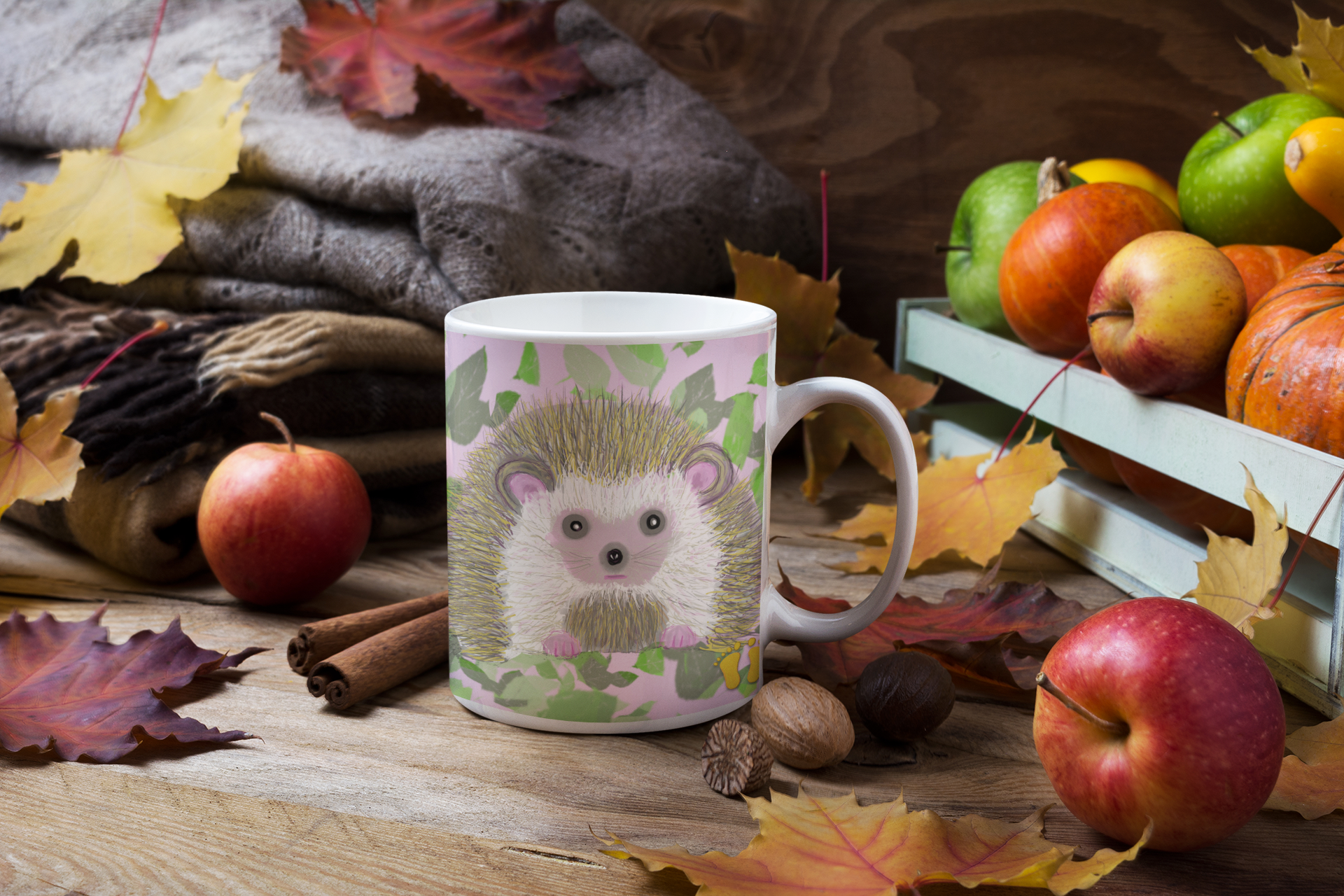 Premium ceramic coffee mug is a unique gift for animal lovers. Brightly colored hedgehog is on a field ofpink and green. Shown here on a table on fall table with apples and leaves